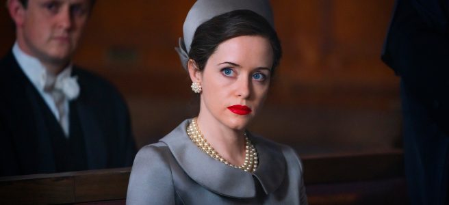 The Duchess of Argyll (Claire Foy) sat on a wooden bench in court. She's wearing a grey/silver coat with a big collar, a matching hat, and a three strand pearl necklace. Her eyes are a piercing blue. Behind her sits an out-of-focus lawyer, wearing a powdered wig.